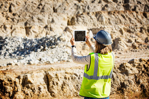 Rear view of female architect in protective workwear photographing quarry through digital tablet